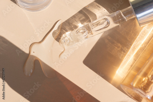 close up of pipette with pouring liquid serum with golden bottle and shadows photo