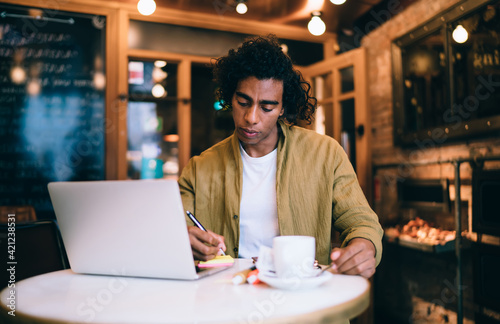 Focused ethnic freelancer taking notes in cafe
