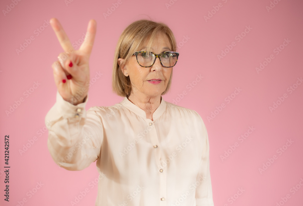 Happy senior woman with victory sign isolated over pink background.