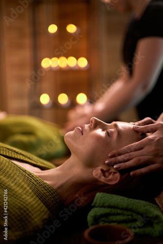 wellness  beauty and relaxation concept - side view on woman lying on bed having face and head massage at spa