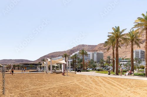 View of the beach on the Ein Bokek embankment on the coast of the Dead Sea, tourist hotels and sandy mountains in the background, in Israel © svarshik