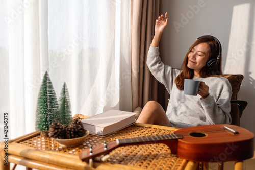 A beautiful young asian woman enjoy drinking coffee and listening to music with headphone at home