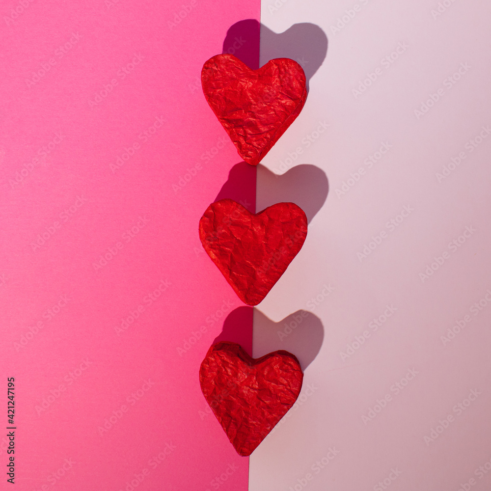 Three red paper hearts on a pastel pink background. Minimal concept.