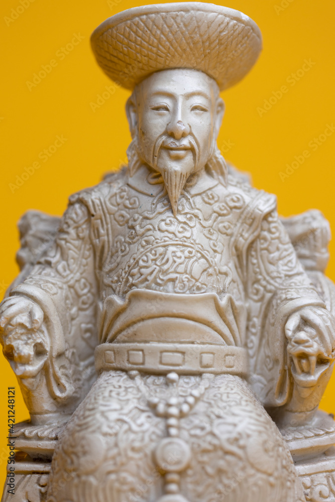 Sitting small emperor sculpture figurine in stately . Studio souvenir still life against a seamless yellow background.