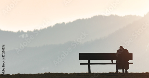 Alone man sits on bench beside mountain sunset evening.