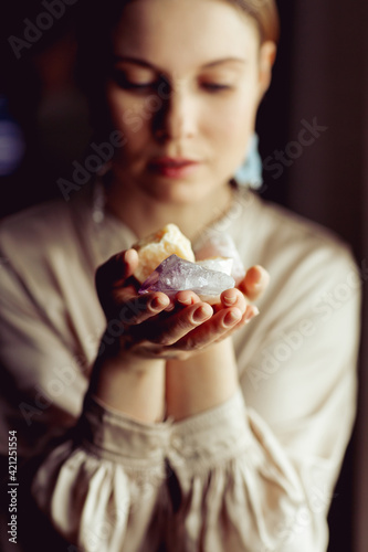 Young european girl holding a gemstone with boths hands in front of her. Mystical woman. Occult  witchcraft scene. Close up paranormal portrait.