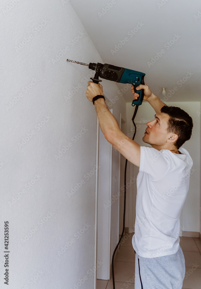 Husband for hour home repairing service. Portrait of handyman drilling a hole in wall to put the painting on. Husband for hour home repairing service. Portrait of handyman drilling a hole in wall to put the painting on.