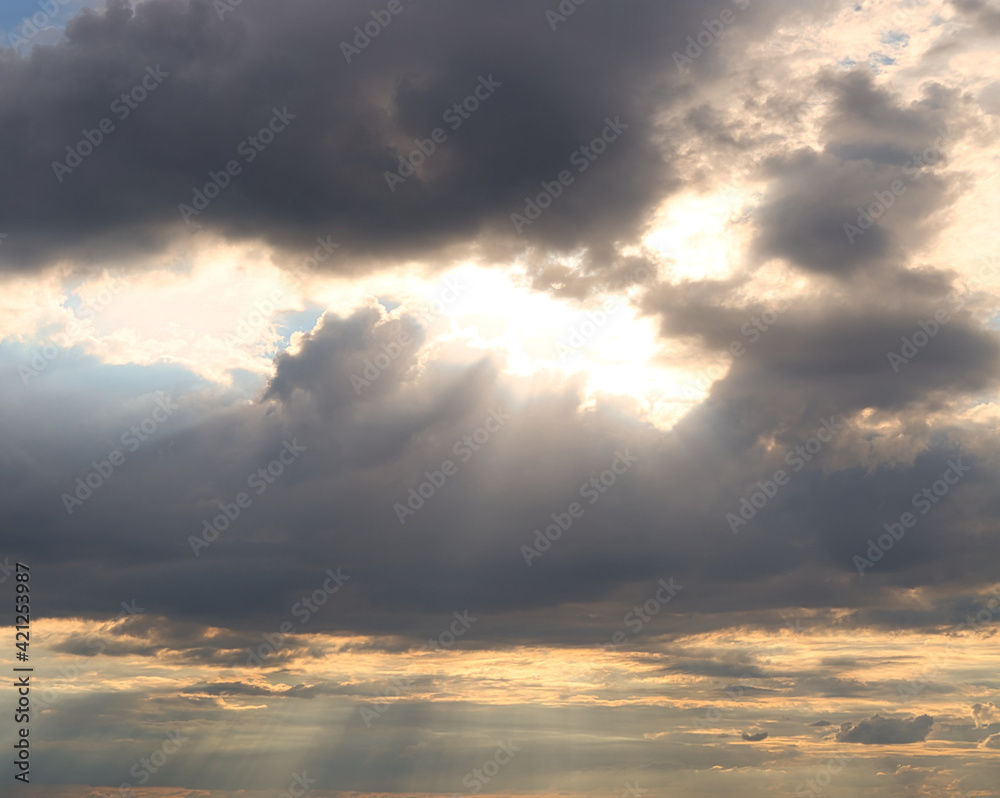 dramatic dark sky with rays and white clouds at sunset