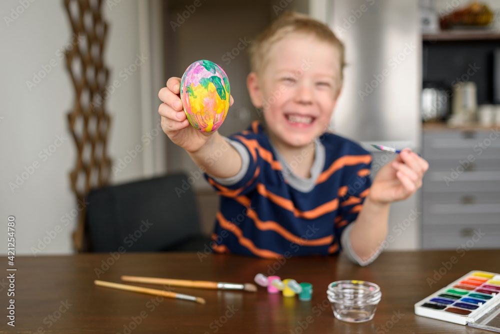 Fototapeta premium Happy smiling Boy coloring Easter egg at home with acrylic paint. Little artist, hobby
