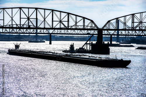 Towboat pushing dry bulk cargo barge under bridges up Mississippi River. Shipping grain corn during harvest season, cargo, food, raw, transportation, agriculture, agricultural, tow, marine, maritime photo