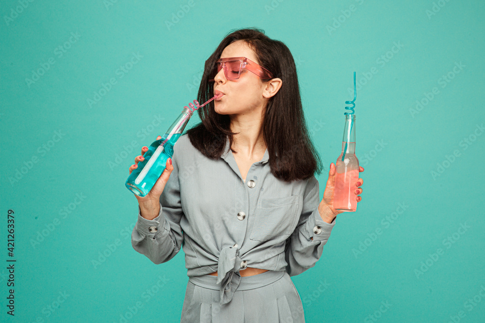 Photo of attractive lady in sunglasses drinks cocktails. Wears grey shirt, isolated turquoise color background Photo of attractive lady in sunglasses drinks cocktails. Wears grey shirt, isolated turquoise color background