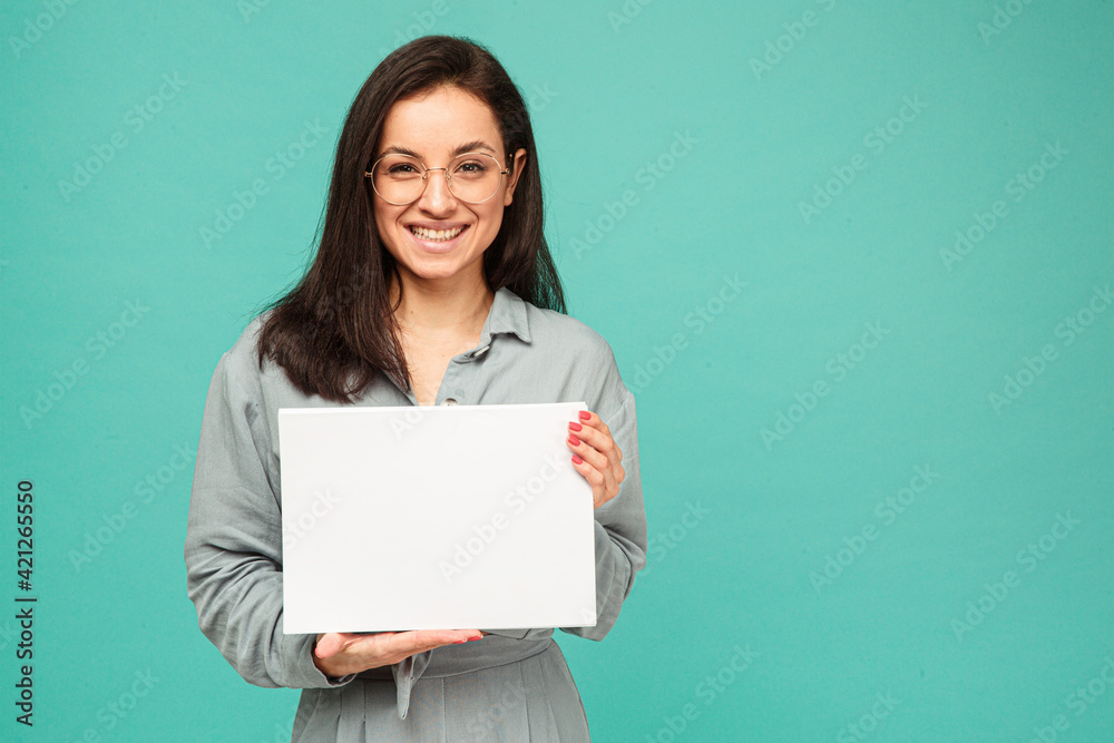 Photo of cute female in glasses holds papers. Wears grey shirt, isolated turquoise color background