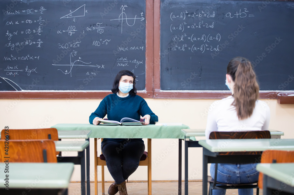 Students in protective face masks studying in classroom with teacher. Precautions in coronavirus pandemic