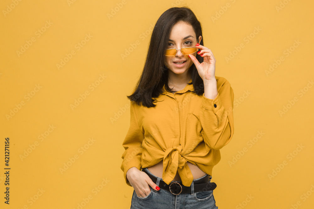 Photo of young female wears sunglasses and looks sexy. Wears yellow shirt, isolated yellow color background Photo of young female wears sunglasses and looks sexy. Wears yellow shirt, isolated yellow color background