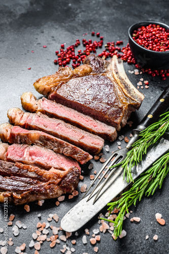 Ribeye steak on the bone with salt and pepper. Grilled Beef meat. Black background. Top view