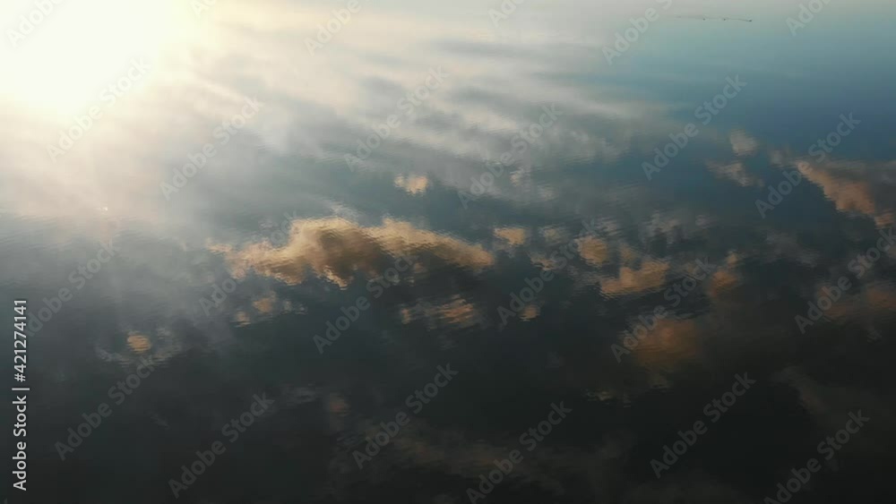 Beautiful aerial cinematic background, drone flying over clouds and sun reflecting in lake with amazing rippled water.