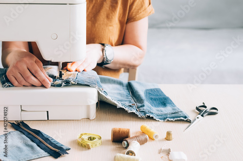 A woman tailor works at sewing machine sews reuses fabric from old denim clothes Fototapet