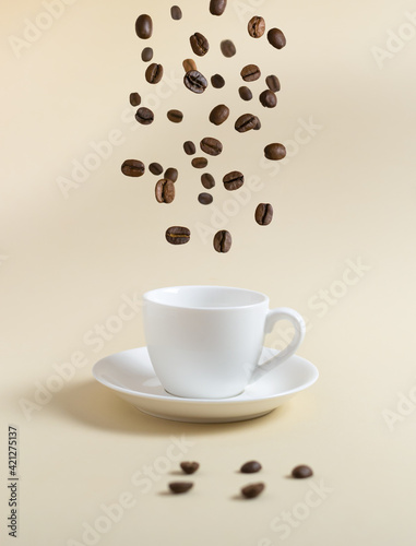 Coffee beans are flying into a white espresso cup on a yellow background. Flying food concept.