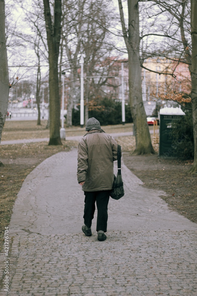 old man with a bag walking the path between the trees in the city park forest old man with a bag walking the path between the trees in the city park forest