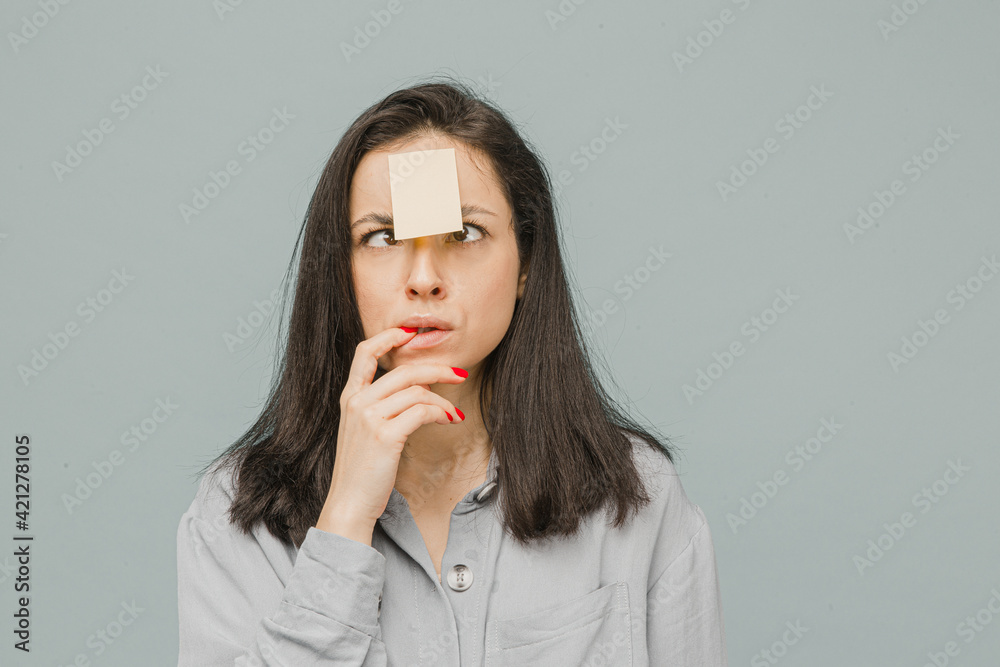 Photo of cute smiling female with sticker over her forehead. Wears grey shirt, isolated grey color background Photo of cute smiling female with sticker over her forehead. Wears grey shirt, isolated grey color background