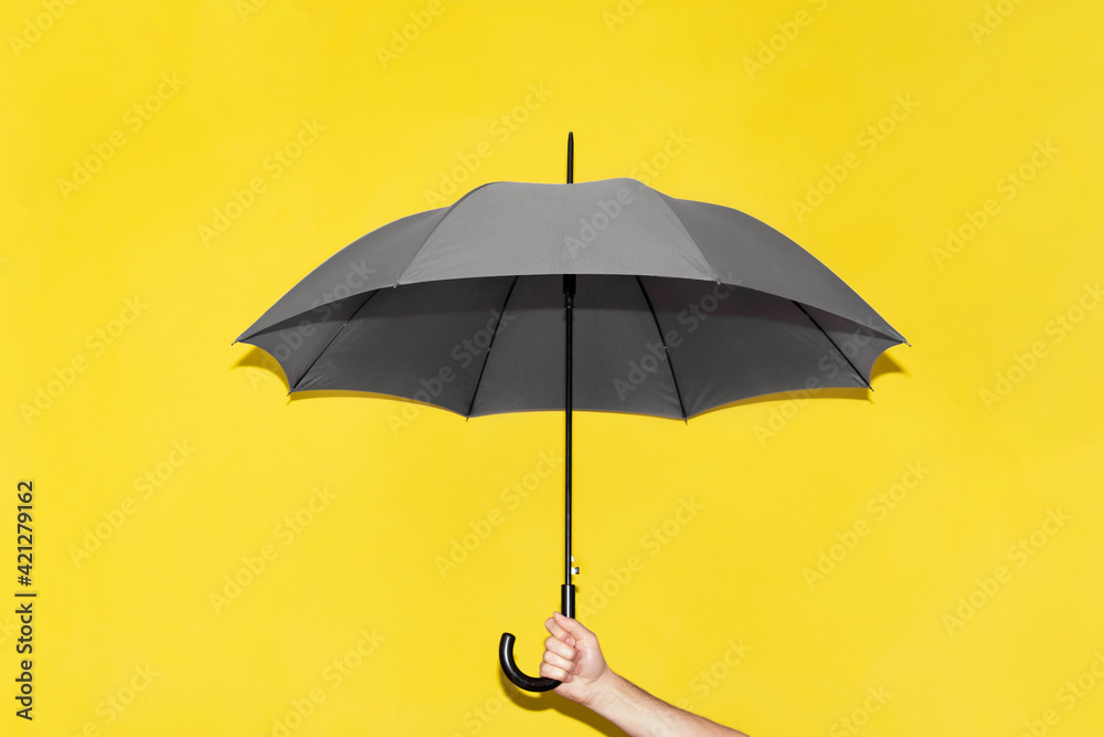 A man holds in his hand a gray umbrella against the background of a yellow wall.