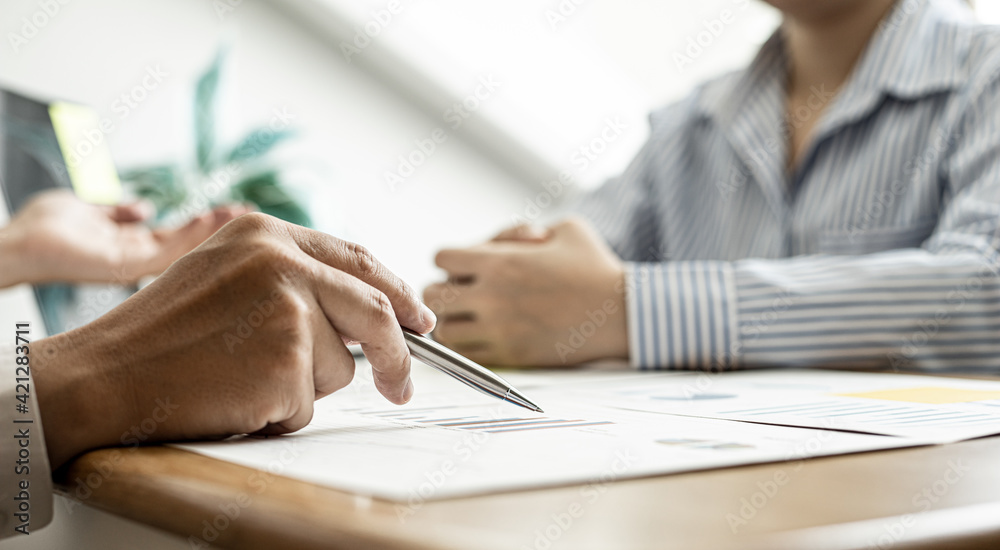 A close-up of a financial businessman holding a pen and pointing at the information sheet on his desk, reading the company's financials to make a financial plan. Financial concept. A close-up of a financial businessman holding a pen and pointing at the information sheet on his desk, reading the company's financials to make a financial plan. Financial concept.