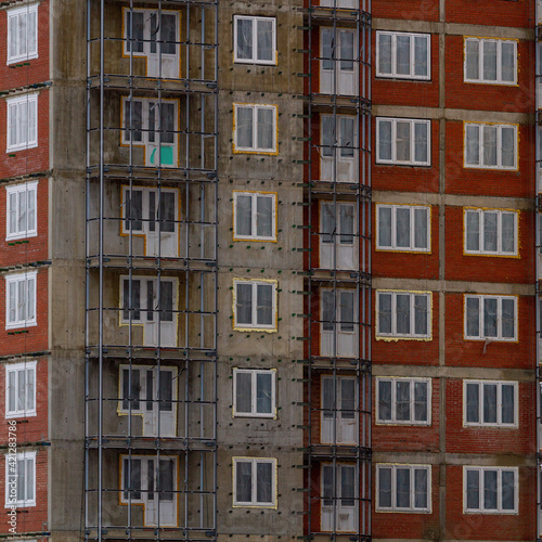 Construction of a residential multi-storey building. Windows, balconies. Concrete, brick walls. Metal structures.
