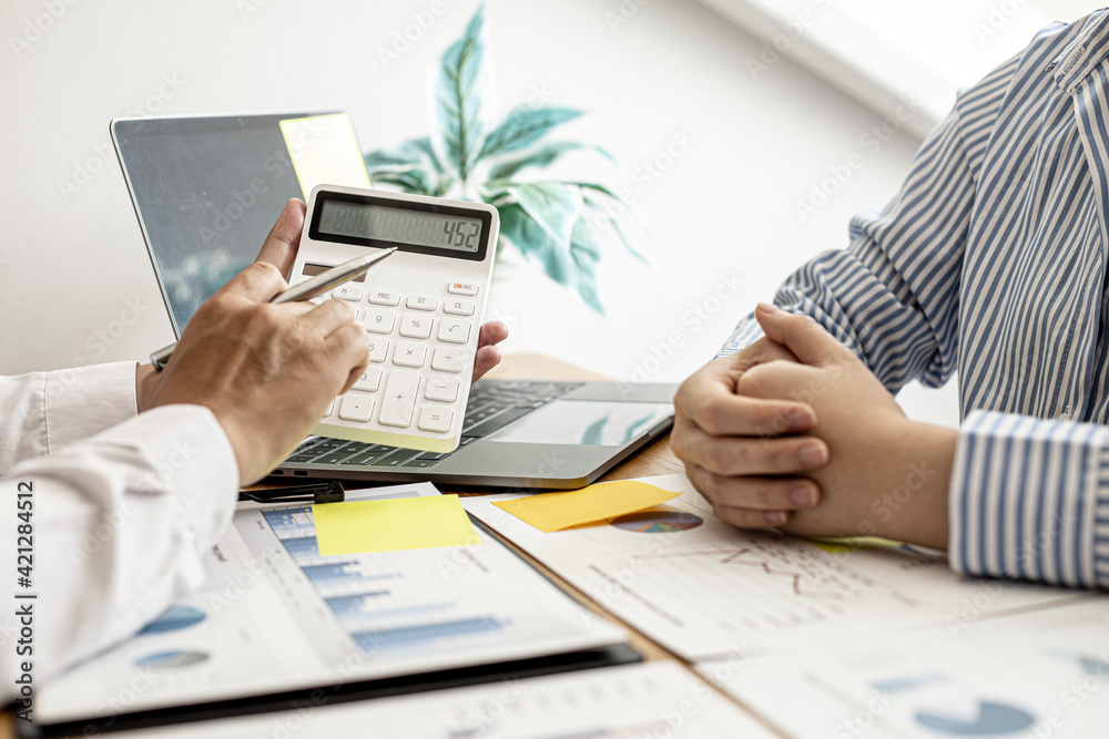 A business man using a calculator to check company financial information Together with business partners, they are having a brainstorming meeting planning to grow the company. Financial concept. A business man using a calculator to check company financial information Together with business partners, they are having a brainstorming meeting planning to grow the company. Financial concept.