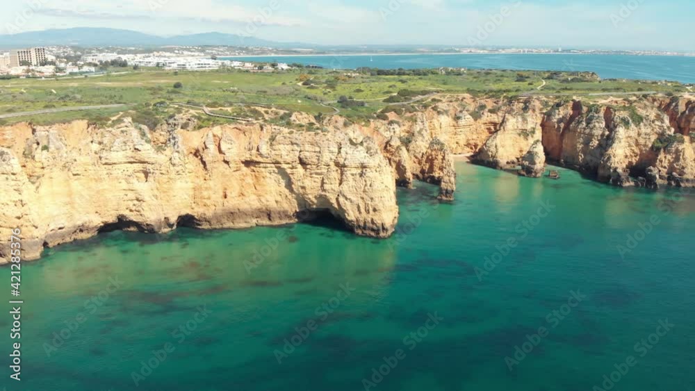 Steep rocky outcrops and calm emerald water in Lagos Algarve, Portugal - Wide Aerial establishing shot Steep rocky outcrops and calm emerald water in Lagos Algarve, Portugal - Wide Aerial establishing shot