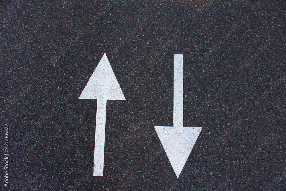 Pointers are two white arrows on an asphalt road, pointing in two directions. Decision making and choice. Pointers are two white arrows on an asphalt road, pointing in two directions. Decision making and choice.