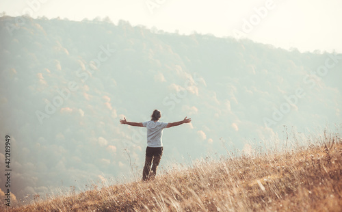 A man stands against the backdrop of a mountain landscape with his hands raised high. Autumn, sun, dawn.