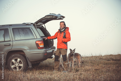 Wallpaper Mural An adult man stands near a car with two dogs against the background of the sky. Traveling with pets. Torontodigital.ca