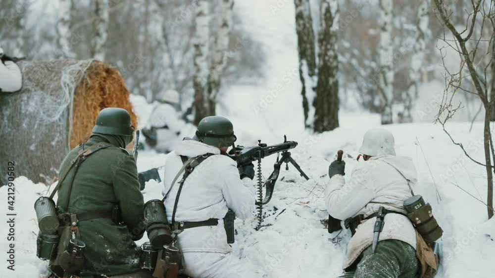 Men Dressed As German Wehrmacht Infantry Soldiers In World War II Hidden Sitting With Weapon In An Ambush And Aiming a Machine Gun at Enemy From Trench In Winter Day. Slow Motion Men Dressed As German Wehrmacht Infantry Soldiers In World War II Hidden Sitting With Weapon In An Ambush And Aiming a Machine Gun at Enemy From Trench In Winter Day. Slow Motion