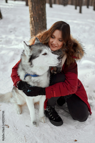 Cute girl in a winter park. A woman plays with a dog. Girl in a red jacket with a hood plays with a husky