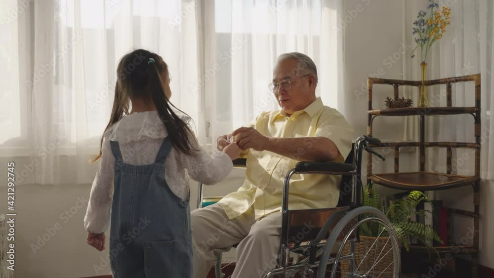 Granddaughter plays with grandpa on a wheelchair. Joyfully the two smiled and happily hugged. Asian Thai family granddaughter and grandfather playing paper birds. tease, laugh and cheer, Retirement, Granddaughter plays with grandpa on a wheelchair. Joyfully the two smiled and happily hugged. Asian Thai family granddaughter and grandfather playing paper birds. tease, laugh and cheer, Retirement,