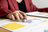 A close-up of a business woman holding a pen and examining the monthly sales document summarized by the sales department, she is analyzing and planning to increase sales. Sales management concept.