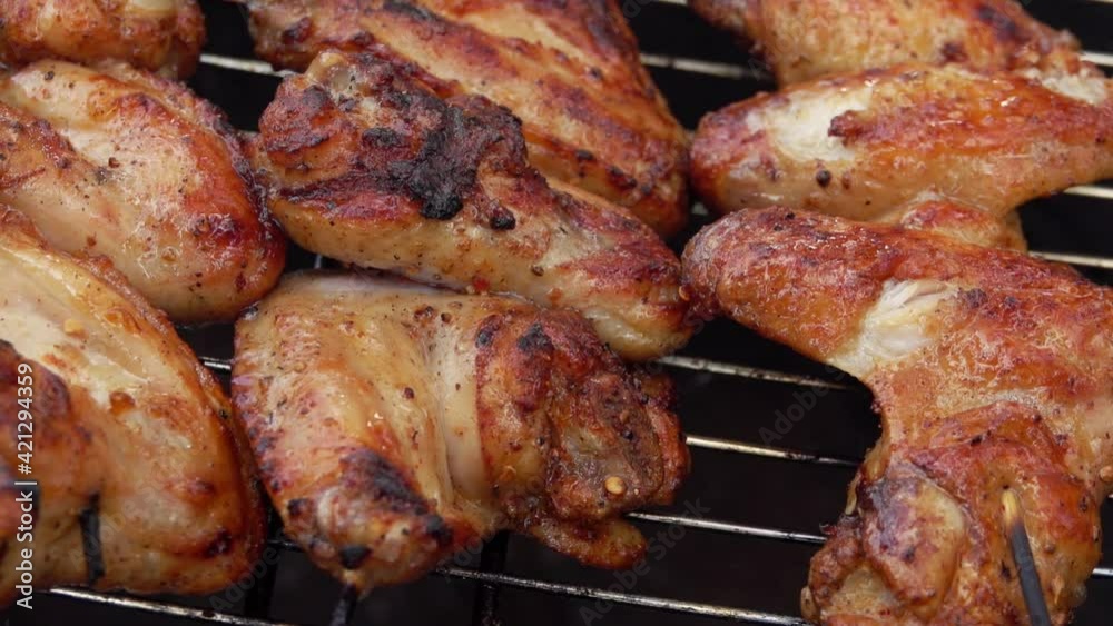 Close-up of the tasty chicken wings rotated on the grill grid with metal tongs outdoors Close-up of the tasty chicken wings rotated on the grill grid with metal tongs outdoors