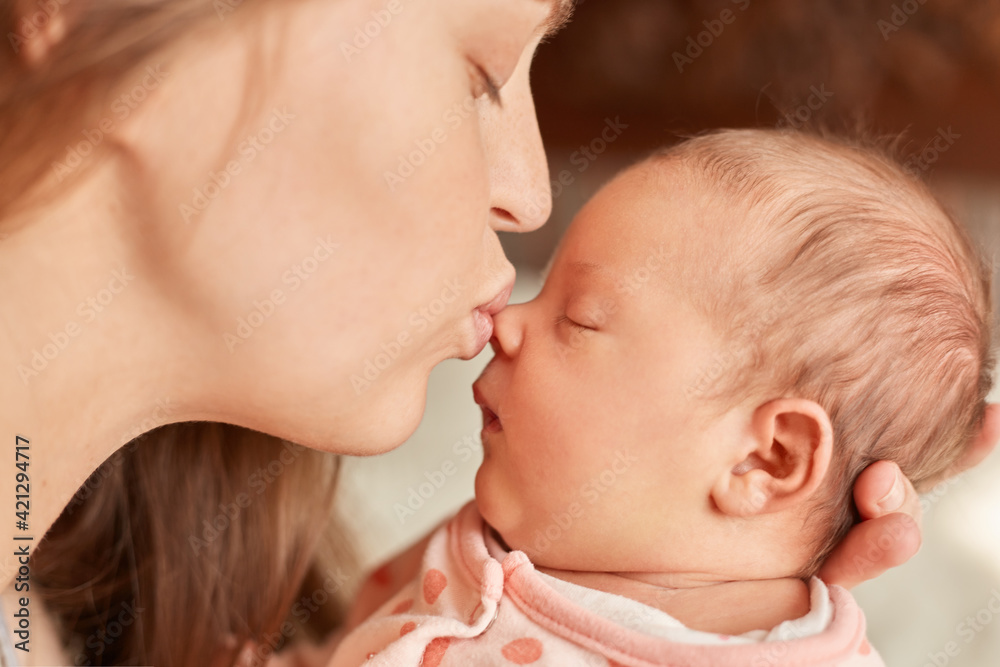 Mom with newborn baby posing indoor, mother kissing her sleepy infant, female closed eyes and pout lips, enjoying spending time with her child, motherhood. Mom with newborn baby posing indoor, mother kissing her sleepy infant, female closed eyes and pout lips, enjoying spending time with her child, motherhood.