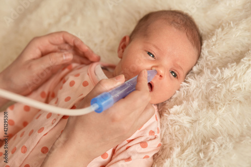 Canvas Print Little baby lying on bed on fluffy blanket, faceless mother using nasal aspiration for taking care of her new born child