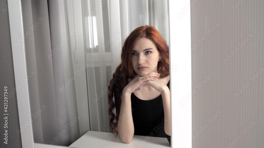 An attractive young red-haired girl looking at her reflection in the mirror
