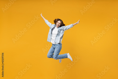 Full length of young overjoyed excited fun expressive student happy woman 20s wearing denim shirt white t-shirt with outstretched hands jump high isolated on yellow color background studio portrait