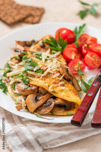 Omelet with mushrooms close-up. Tasty breakfast or lunch. Omelet with champignons, cheese, and tomatoes in a white plate on the table. 