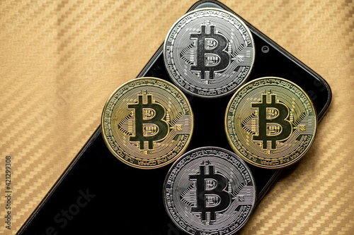 Moedas de bitcoin douradas e prateadas em cima de aparelho celular desligado. Quatro tokens de criptomoedas com fundo dourado desfocado. photo