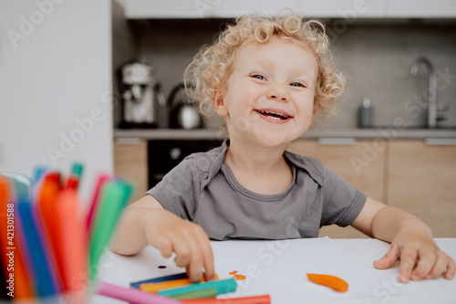 Portrait of smiling pre-school girl sitting at her kitchen table playing with plasticine. The cute lovely girl is spending his afternoon free time at home.