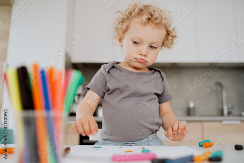 Portrait of a pre-school girl sitting at her kitchen table playing with plasticine. The cute lovely girl is spending his afternoon free time at home.