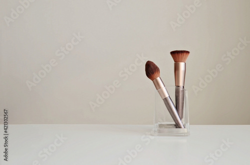 Makeup brushes in a glass stand on a white background, copy space. Interior beauty mockup.