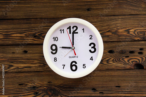 A white clock showing the time on a wooden wall