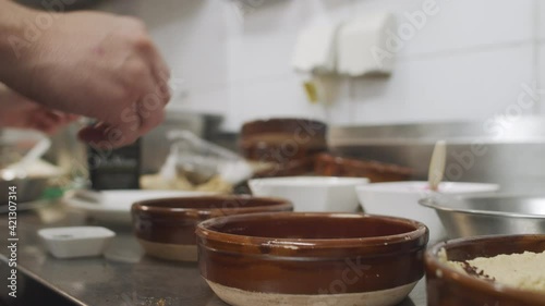 Chef plating the dish in restaurant kitchen, adding spices into small ceramic bowl. Close up slow motion shot. photo