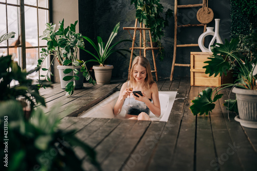 Beautiful young woman drinking champagne and looking to the smart phone enjoying bubble bath photo