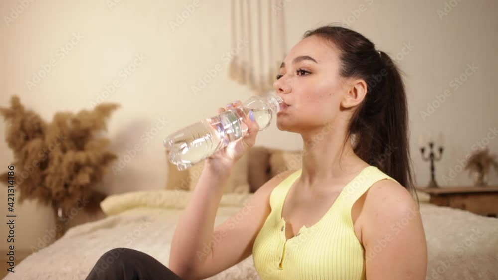A young beautiful girl drinks water from a bottle, smiles, rest after a workout. Sportswear, interior, home. A young beautiful girl drinks water from a bottle, smiles, rest after a workout. Sportswear, interior, home.